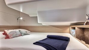 A modern hotel room with a bed, a nightstand, a wall-mounted lamp, and a shelf with books. - Sun-kissed Sailing Adventure in Split-Dalmatia, Croatia (Trogir)