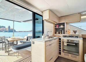 A compact kitchen with a built-in stove, a sink, and a dining area with a bench and chairs. - Sun-kissed Sailing Adventure in Split-Dalmatia, Croatia (Trogir)