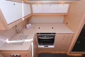 Una kitchenette compacta con horno integrado, un lavamanos y armarios de almacenamiento.