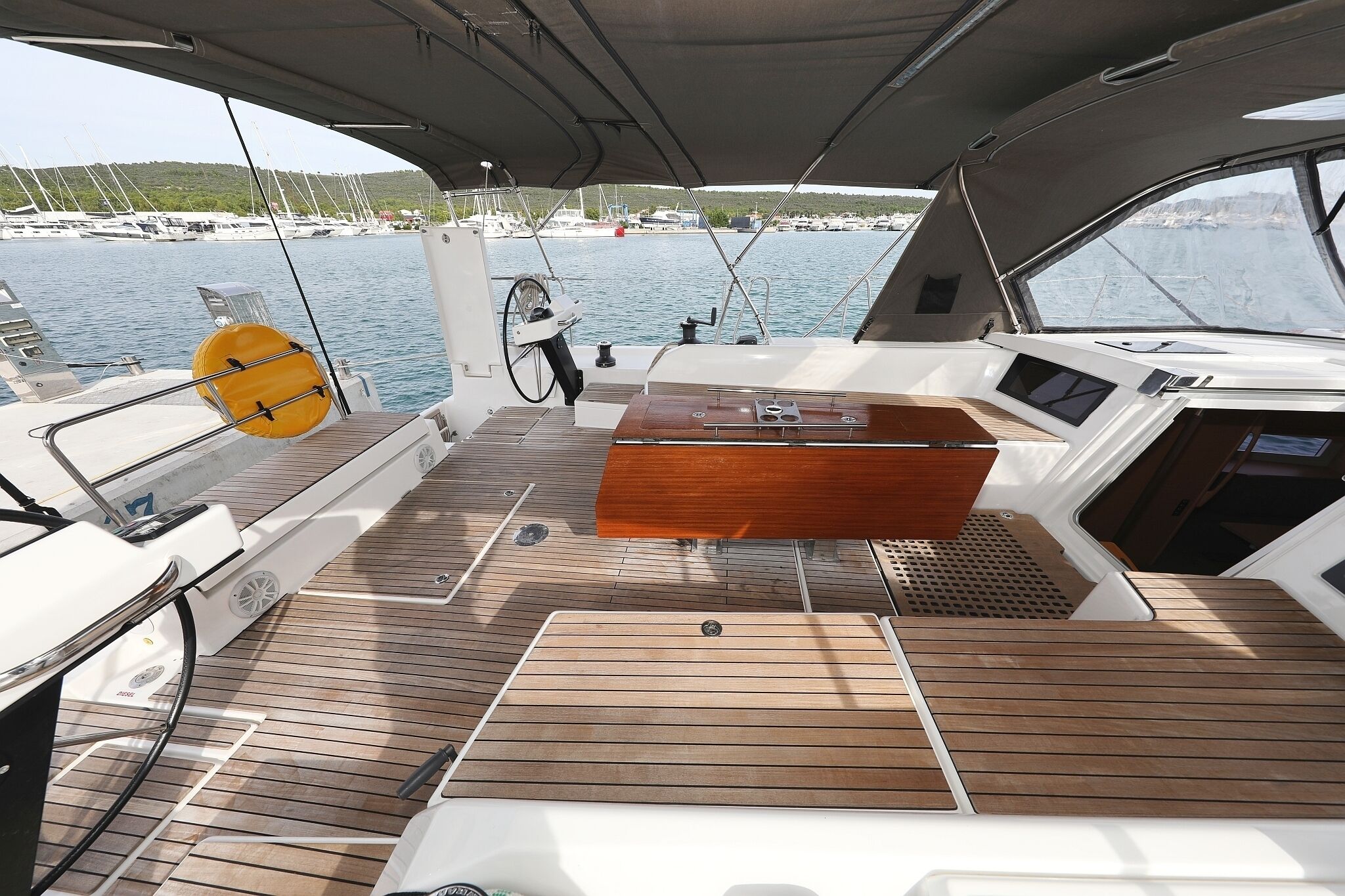 A boat deck with a wooden floor, a central console, and a view of the marina.
