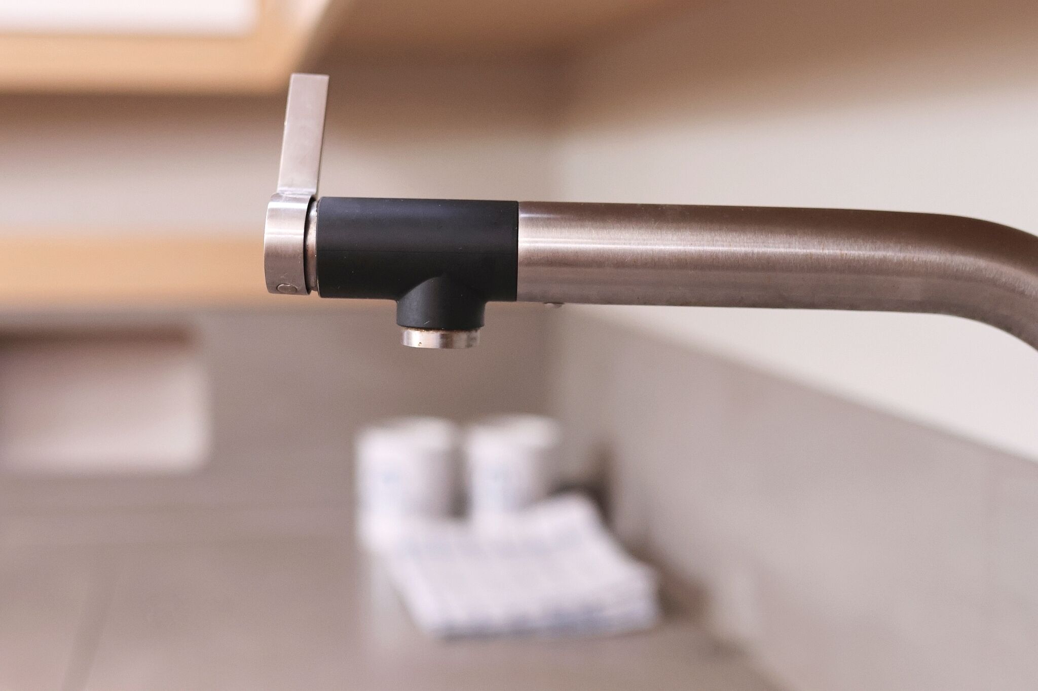 A close-up of a metallic faucet with a black handle, a white towel, and a blurred background.