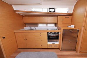 A compact kitchen with wooden cabinets, a built-in oven, and a small refrigerator. - Sun-kissed Sailing Adventure in Split-Dalmatia, Croatia (Trogir)
