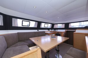 A cabin with a central table, cushioned seating, a control panel, and windows with curtains. - Sun-kissed Sailing Adventure in Split-Dalmatia, Croatia (Trogir)