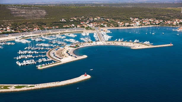 An aerial view of a marina with numerous boats docked, a lighthouse, and a coastal town in the background. - Sun-Kissed Sailing Adventure in Zadar, Croatia (Bibinje)