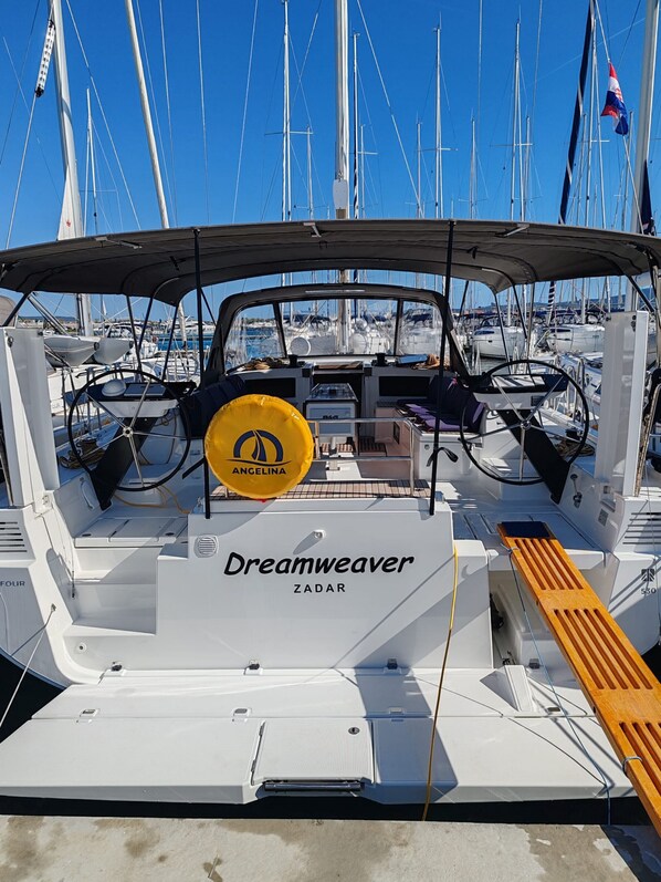Un barco llamado 'Dreamweaver' con un timón, un flotador amarillo y cubierta de madera.