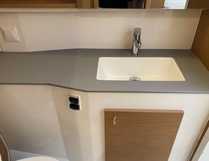 Eine kleine Küche mit Spüle, Wasserhahn und einem Holzschrank.