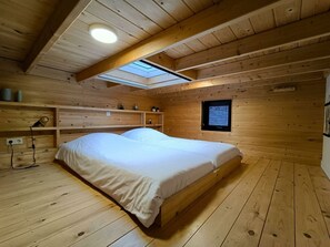 Quarto de cabana de madeira com claraboia, uma cama e uma pequena janela.