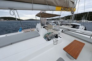 Una barca a vela con un cartello 'ANCELINA', una zona relax imbottita e un ponte in legno.