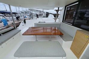 Ein Bootsdeck mit Holztisch, gepolsterten Sitzgelegenheiten und einem Fenster.