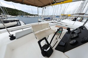 A boat deck with a cushioned seat, control panel, and a view of a marina with multiple boats. - Sibenik Sun and Beach Sailing Extravaganza: A Croatian Coastal Adventure (Vodice)