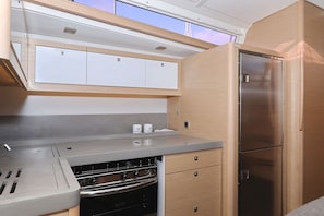 A compact kitchen with a built-in oven, a stainless steel refrigerator, and wooden cabinets. - Sun-Kissed Sailing Adventure in Zadar, Croatia (Biograd na moru)