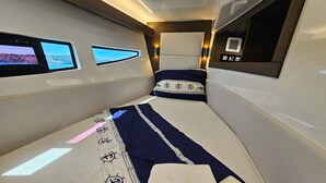 Une petite cabine étroite, bien éclairée, avec un lit, une petite fenêtre et un panneau de commande.