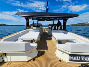 A boat deck with two white cushioned seating areas, a central table, and a flagpole with a flag. - Sun-kissed Sailing Adventure in Split-Dalmatia, Croatia (Seget Donji)