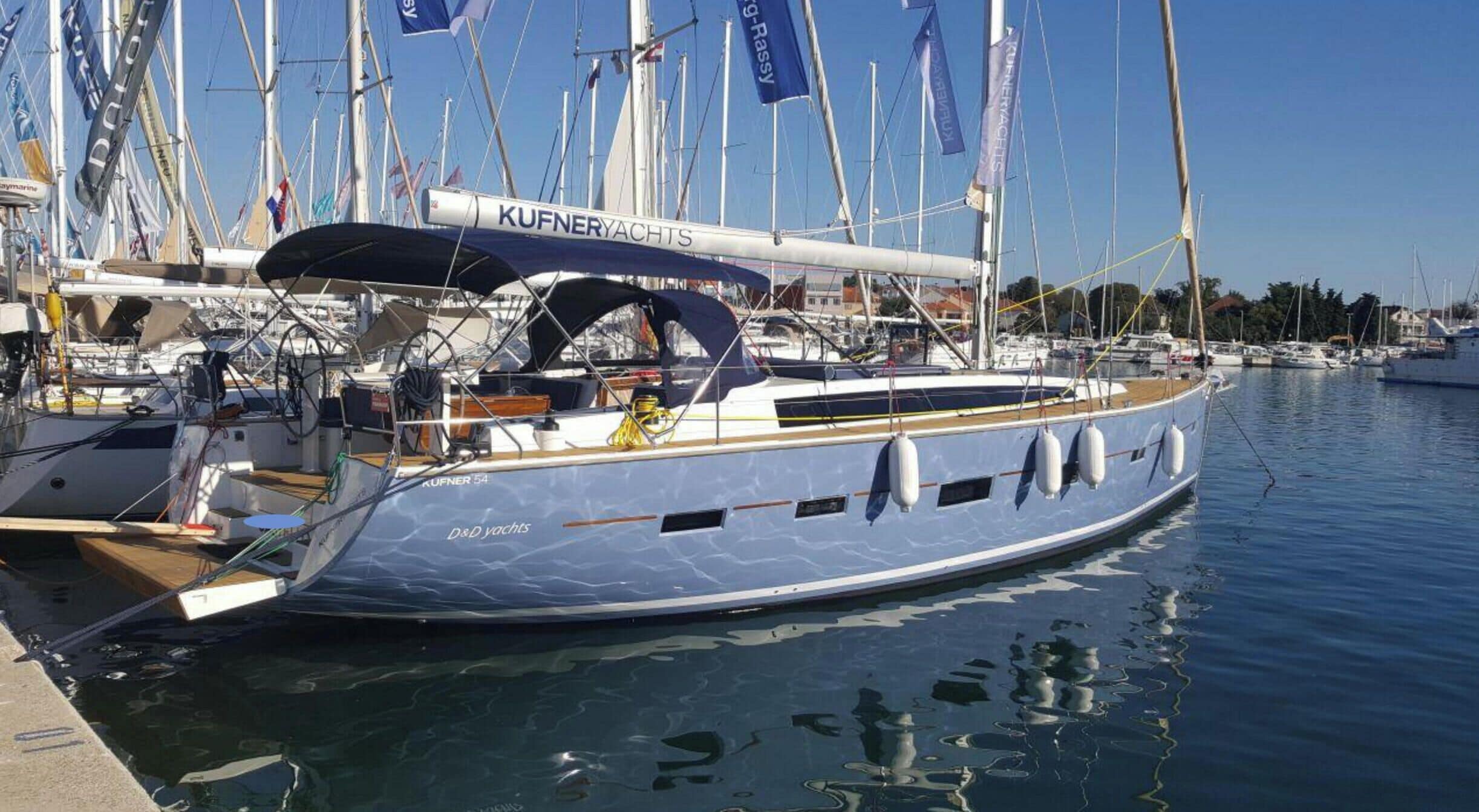 Eine Segelyacht liegt im Hafen, mehrere Flaggen wehen und der Himmel ist wolkenlos.
