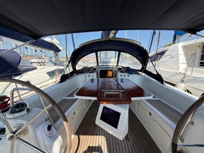 A boat deck with a wooden table, a steering wheel, and a small screen.