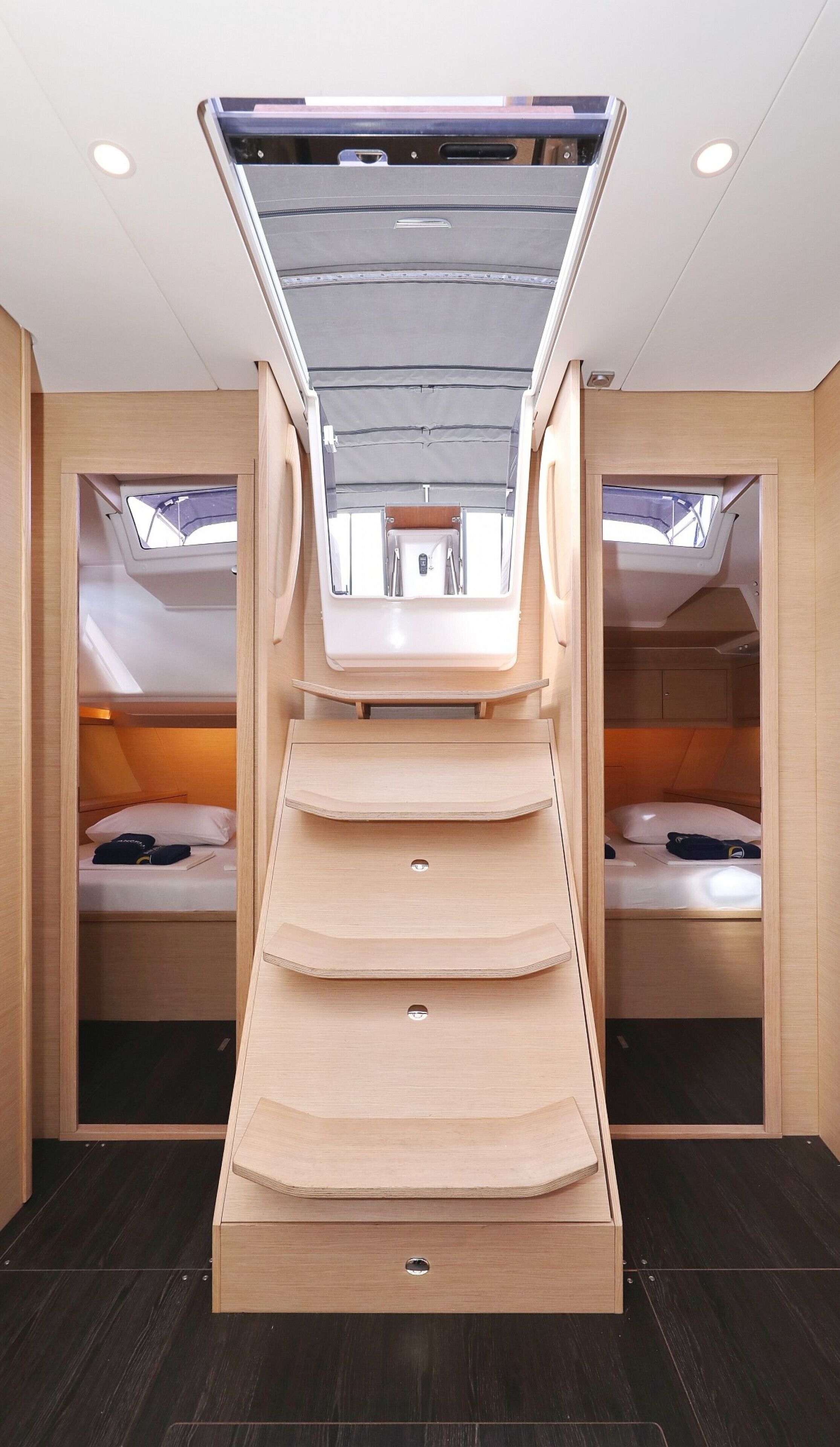 A compact, well-lit interior with a central staircase leading to a loft area, two sleeping areas with skylights, and a small kitchenette.