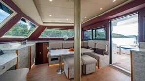 A yacht interior with a dining area, cushioned seating, a table with a vase, and large windows offering views of the water. - Sun-Kissed Sailing Adventure in Split, Croatia (Split)