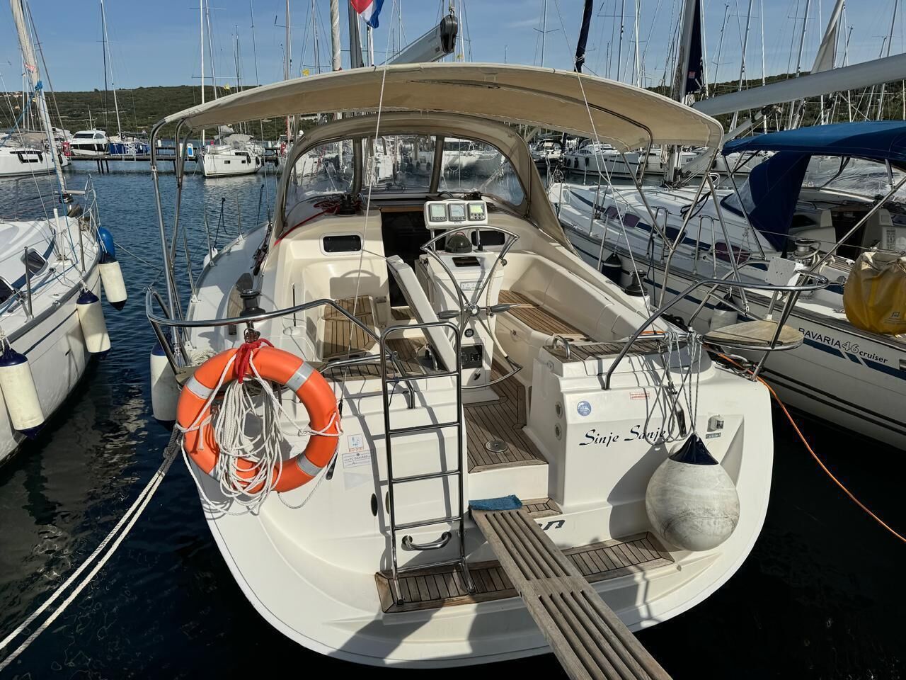 Een boot afgemeerd in een jachthaven, met een reddingsboei, bedieningspaneel en een kajuit.