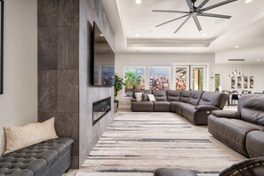 A modern living room with a sectional sofa, a fireplace, a ceiling fan, and a large window. - Mansion includes Free Waterpark Access + Ropes Course Adventure Gift Basket (Hurricane)