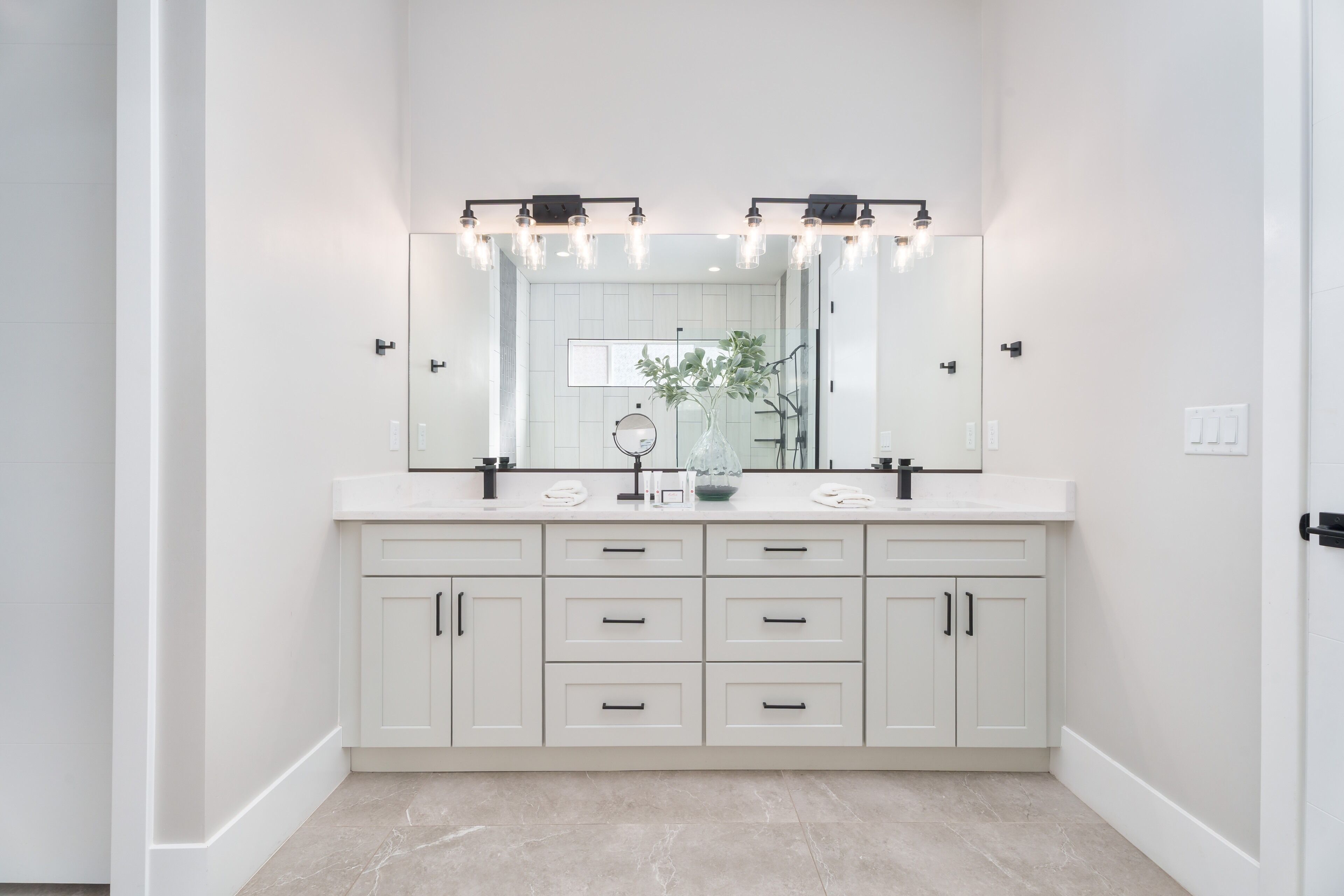 A bathroom with a white vanity, a large mirror, and a light fixture above the mirror.