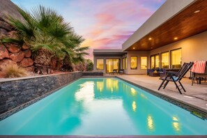 A modern pool area with a stone wall, palm trees, and a sunset sky. - Mansion includes Free Waterpark Access + Ropes Course Adventure Gift Basket (Hurricane)