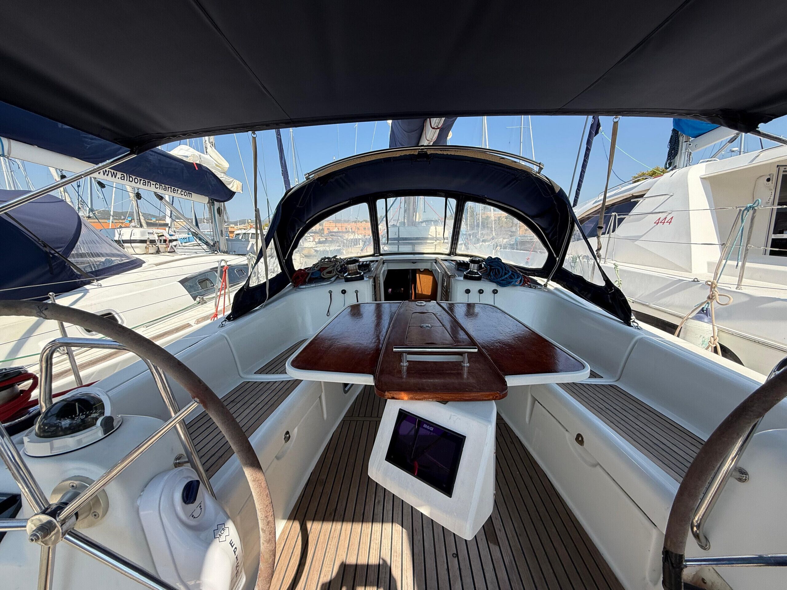 Een scheepdek met een houten tafel, een stuurwiel en een klein scherm.
