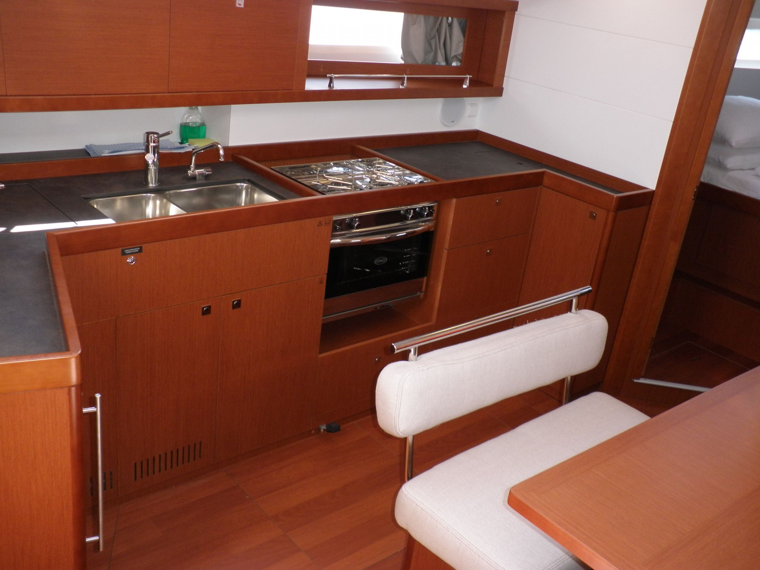 A compact kitchen with wooden cabinets, a stainless steel sink, a stove, and a bench.