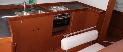 A compact kitchen with wooden cabinets, a stainless steel sink, a stove, and a bench.