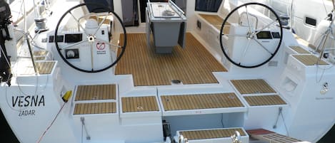 Le pont d’un bateau, avec une zone centrale aménagée en salon, des panneaux de contrôle et le nom « VESNA ZADAR » inscrit sur le côté.