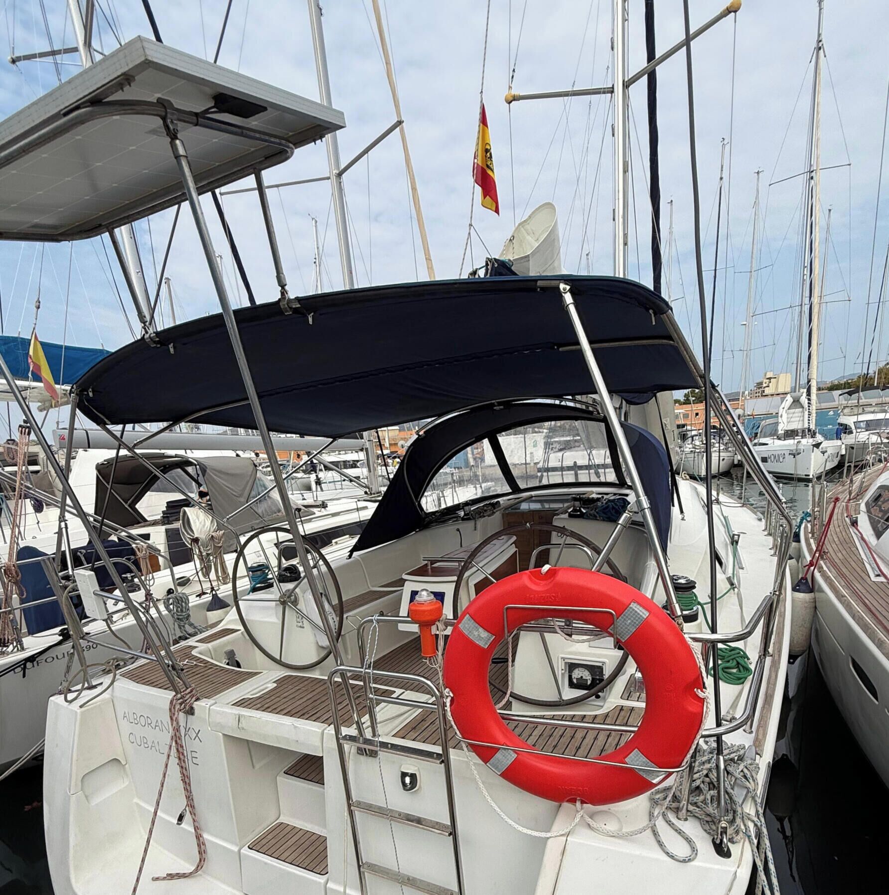 A sailboat docked at a marina with a lifebuoy, steering wheel, and a canopy.