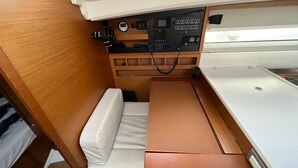 Um espaço interior compacto com um banco de madeira, uma mesa pequena e um painel de controle com vários botões e mostradores.