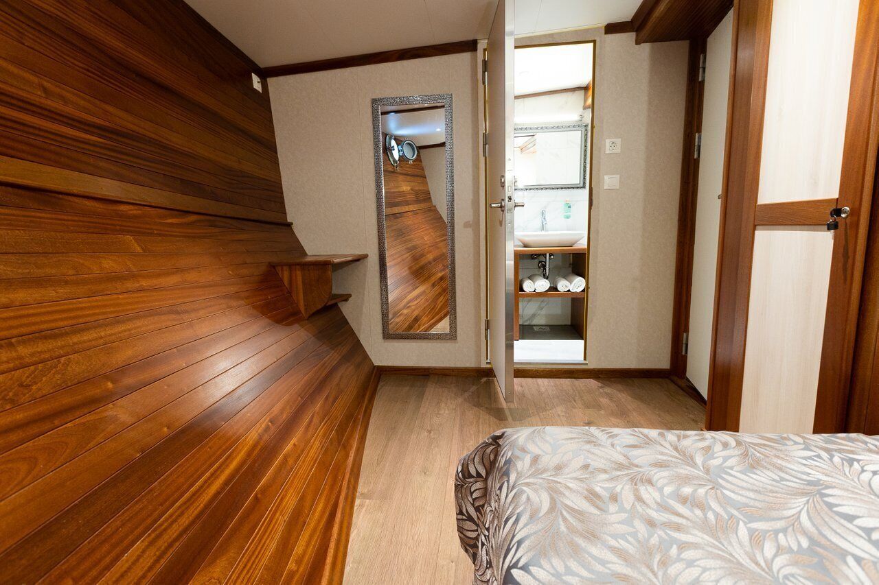 Ein Schlafzimmer mit Holzboden, einem Bett mit gemustertem Überwurf, einem Spiegel und einem Badezimmer mit Waschbecken und Regalen.