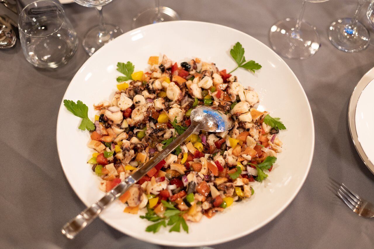 Ein Teller gemischter Salat mit verschiedenen Gemüsesorten und einem Löffel auf einer Tischplatte.