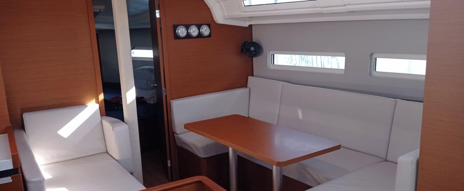 Espaço interno aconchegante com mesa de madeira e assentos acolchoados brancos.