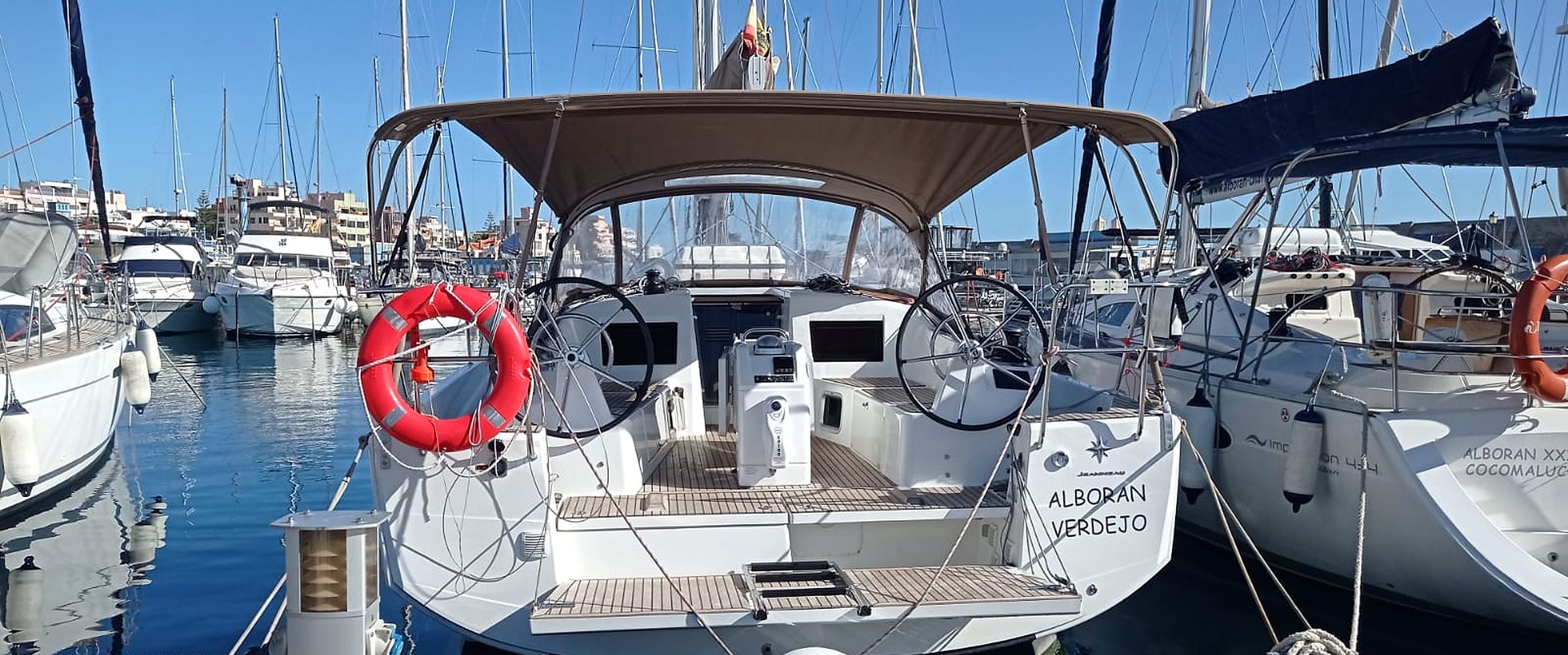 A marina with multiple boats docked, featuring lifebuoys, a steering wheel, and a cabin with a view of the water.