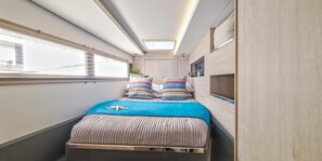 A narrow, well-lit room with a bed, a skylight, and a window.