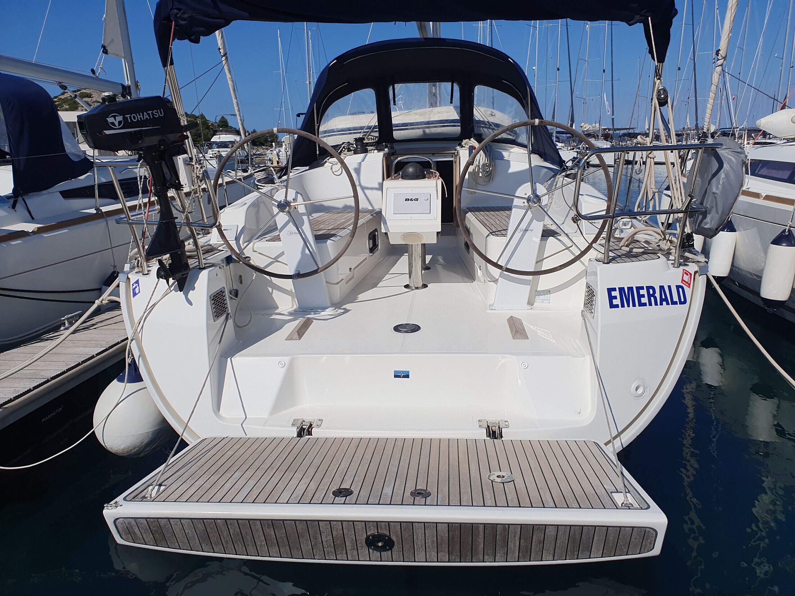 A boat named 'EMERALD' docked at a marina with multiple boats, a steering wheel, and a winch.