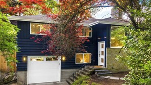 A two-story house with a white garage door, a front entrance with a small porch, and a staircase leading to the second floor. - Lake City 5BR Retreat, Hot Tub, 2 Fire Pits, EV, Sleeps 10 (Seattle)