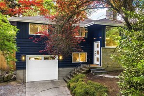 A two-story house with a white garage door, a front entrance with a small porch, and a staircase leading to the second floor. - Lake City 5BR Retreat, Hot Tub, 2 Fire Pits, EV, Sleeps 10 (Seattle)