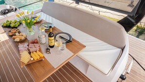 A boat deck with a dining area featuring a wooden table with food and drinks, a cushioned bench, and a view of the water. - Sun-Kissed Sailing Adventure in Zadar, Croatia (Bibinje)