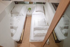 Ein Zimmer mit zwei Betten, jeweils mit ordentlich gefalteten weißen Handtüchern, einem kleinen Tisch mit einer Pflanze und Holzboden.