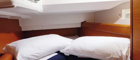 Una cama compacta con ropa de cama blanca y azul oscuro, un cabecero de madera y una ventana arriba.
