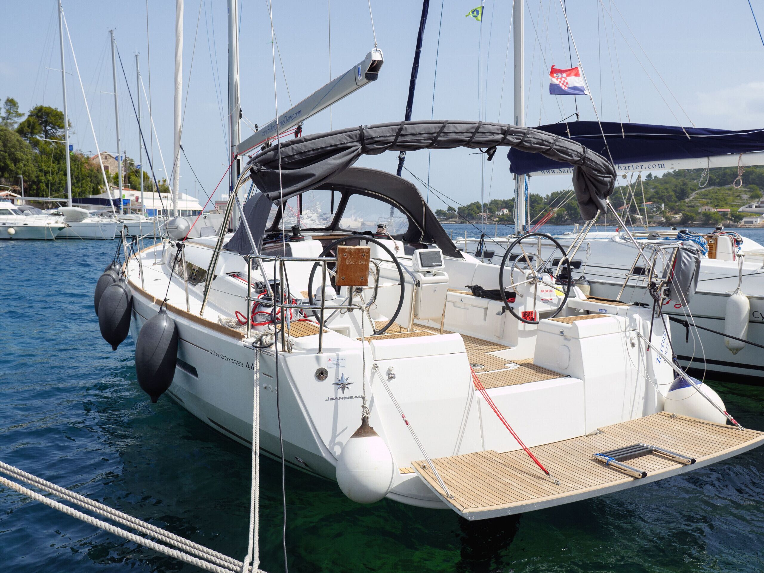 Een zeilboot afgemeerd in een jachthaven, met vrij uitzicht op het water, een stuurwiel en een klein dek met zitplaatsen.