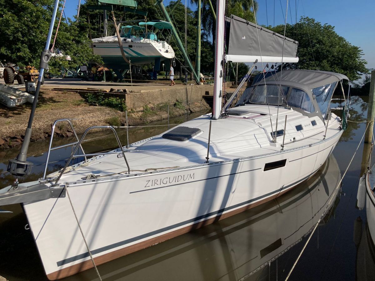 Un velero blanco llamado 'ZIRIGUIDUM' atracado en un puerto deportivo con una zona de cubierta techada.