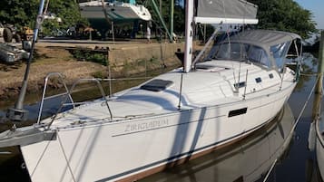 Un velero blanco llamado 'ZIRIGUIDUM' atracado en un puerto deportivo con una zona de cubierta techada.