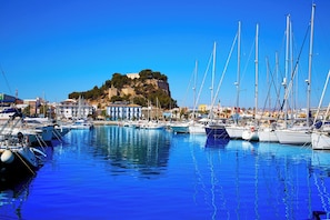 A marina with boats docked, a hill with buildings, and clear blue skies.