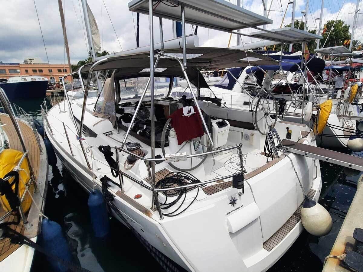 A sailboat docked at a marina with a covered deck area, a winch, and a lifebuoy.