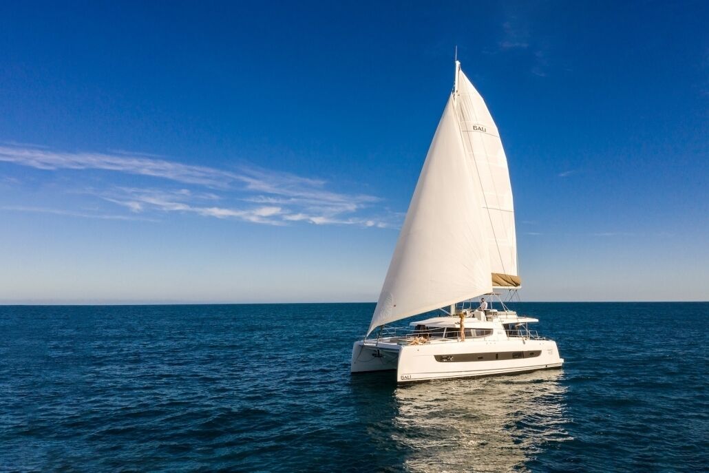 Un velero con vela blanca navegando sobre aguas azules y tranquilas bajo un cielo despejado.