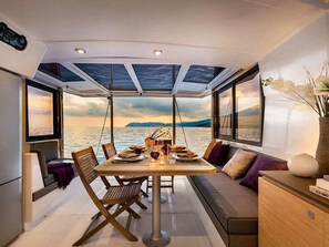 A dining area with a table set for two, a sofa, and a view of the sea. - Caribbean Sun-Kissed Sailing: A Luxurious Beach Experience from Martinica, Le Marin (Le Marin)