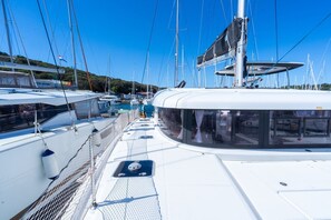 Een jachthaven met meerdere zeilboten die afgemeerd liggen, met een wit dek voorzien van een glazen uitkijkpunt en een overdekt zitgedeelte.